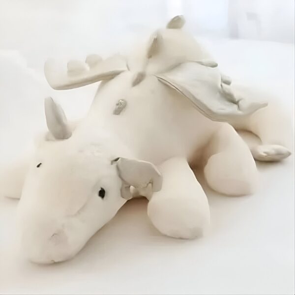 Peluche de dragon blanc avec des ailes grises allongées sur le ventre.