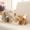 Deux éléphants en peluche, l'un gris et l'autre brun, sont assis sur un canapé. Le plus grand éléphant a de grandes oreilles et une trompe. Le plus petit éléphant a des oreilles roses et une trompe courte.
