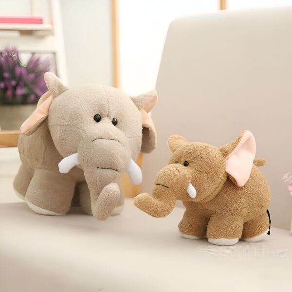 Deux éléphants en peluche, l'un gris et l'autre brun, sont assis sur un canapé. Le plus grand éléphant a de grandes oreilles et une trompe. Le plus petit éléphant a des oreilles roses et une trompe courte.