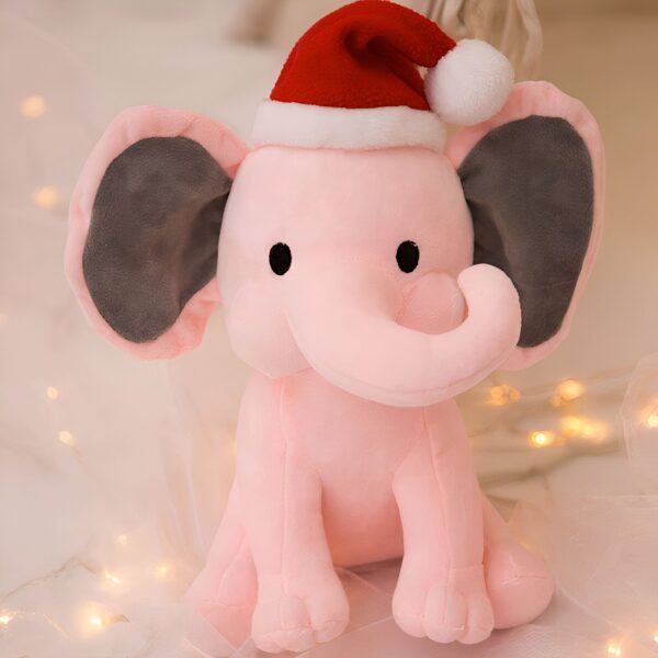 Un éléphant en peluche rose portant un bonnet de Noël rouge assis sur un fond blanc avec des lumières de Noël.