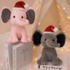 Deux éléphants en peluche portant des chapeaux de Père Noël, un rose et un gris, assis sur un livre.