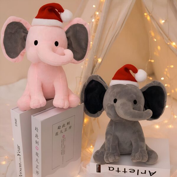 Deux éléphants en peluche portant des chapeaux de Père Noël, un rose et un gris, assis sur un livre.