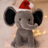 Un éléphant en peluche gris portant un chapeau de Père Noël, assis sur un fond blanc.