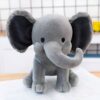 Une peluche d'éléphant gris assis sur un livre. L'éléphant a de grandes oreilles grises et un tronc gris.
