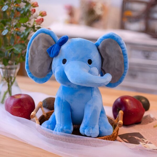 Un éléphant en peluche bleu avec un nœud bleu, assis dans un panier en osier sur une table en bois.