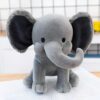 Un éléphant en peluche gris avec de grandes oreilles et une trompe. Il est assis sur un livre.