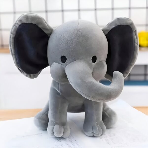 Un éléphant en peluche gris avec de grandes oreilles noires assis sur une surface blanche.