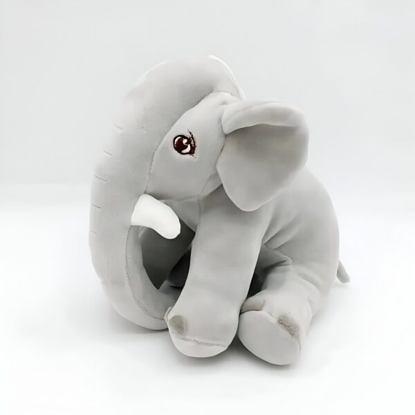 Une peluche d'éléphant gris assise sur un fond blanc.
