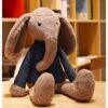 Une peluche d'éléphant gris portant une chemise bleue à rayures est assise sur une table en bois.