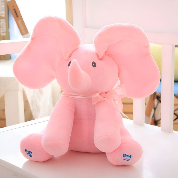 Peluche éléphant rose assis sur une chaise avec un nœud rose et écrit "play" et "sing" sur ses pieds.