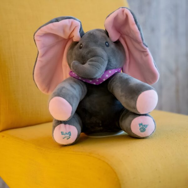 Un éléphant en peluche gris avec des oreilles roses et un foulard violet à pois blancs assis sur un fauteuil jaune.