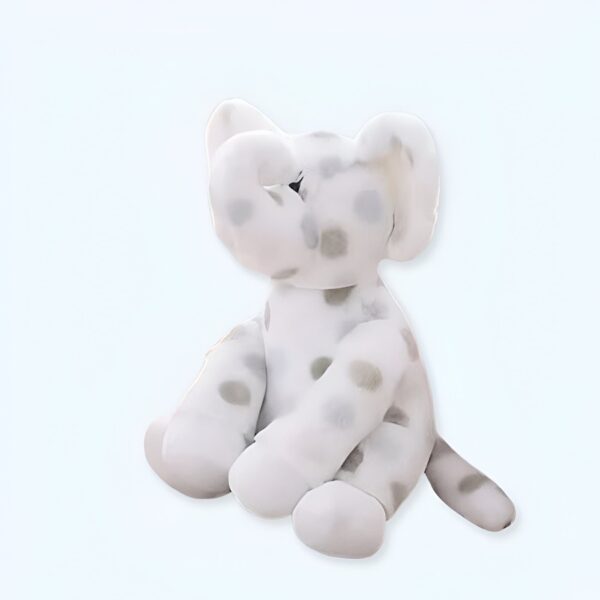 Un éléphant en peluche blanc avec des points gris assis sur un fond blanc.