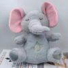 Un éléphant en peluche gris avec des oreilles roses, assis sur un livre. Il a les yeux fermés et un motif de goutte d'eau jaune sur son ventre.