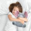 Une jeune fille endormie dans un lit blanc avec une peluche éléphant grise aux oreilles roses.
