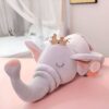 Un éléphant en peluche gris avec une couronne dorée, allongé sur le dos, les yeux fermés. Il est parfait pour les enfants et les bébés.