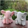 Deux éléphants en peluche, l'un rose et l'autre gris, posés sur un fond en bois.