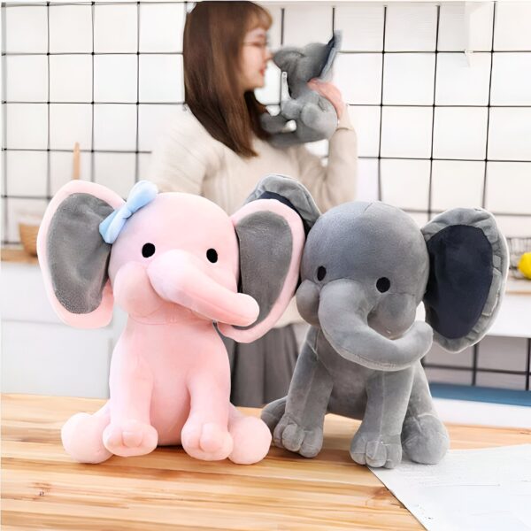 Deux éléphants en peluche, l'un rose avec un nœud bleu et l'autre gris, sur un fond de bois.