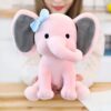 Une peluche rose en forme d'éléphant avec un nœud bleu sur la tête, tenue par une personne.