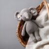 Un éléphant en peluche gris crocheté dans un panier en osier avec un tissu beige.
