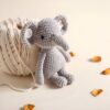 Un éléphant en crochet gris assis à côté d'une pelote de laine beige.