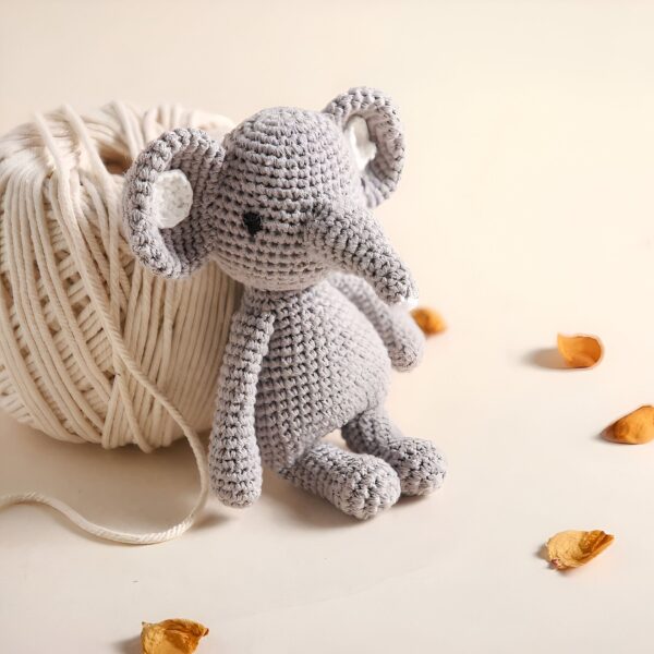 Un éléphant en crochet gris assis à côté d'une pelote de laine beige.