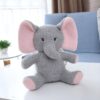 Un éléphant en peluche gris avec des oreilles roses assis sur une table blanche.