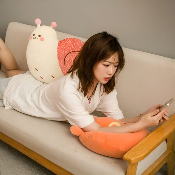 Une jeune femme allongée sur un canapé beige avec deux oreillers en forme d'escargot et d'ours. Elle utilise son téléphone.