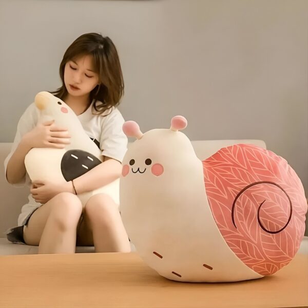 Une jeune femme assise sur un canapé avec une peluche en forme d'oiseau et une autre en forme d'escargot.