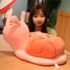 Une jeune femme souriante tenant un grand coussin en forme d'escargot rose.