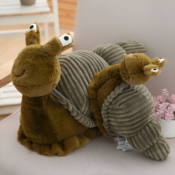 Une peluche en forme d'escargot de couleur beige avec de grands yeux. L'escargot est assis sur un fauteuil en tissu beige.