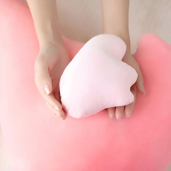 Des mains tenant un cœur en peluche rose sur un fond rose.