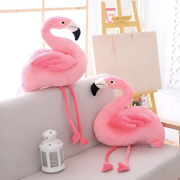 peluche-flamant-rose-jouet-en-peluche-doux-pour-enfant-decoration-chambre-2a Deux peluches flamants roses assis sur un canapé blanc. L'un est assis sur le devant du canapé et l'autre est assis sur le côté. Une lanterne blanche se trouve sur le canapé devant les flamants roses.