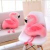 peluche-flamant-rose-jouet-en-peluche-doux-pour-enfant-decoration-chambre-3a Deux coussins en forme de flaman rose, l'un sur un canapé blanc et l'autre sur une chaise blanche.