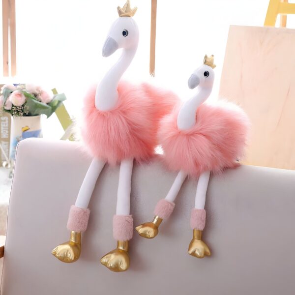 peluche-flamant-rose-princesse-avec-couronne-et-chaussures-dorees-cadeau-enfant-3a Deux peluches de flamants roses avec des couronnes dorées, assises sur un canapé.