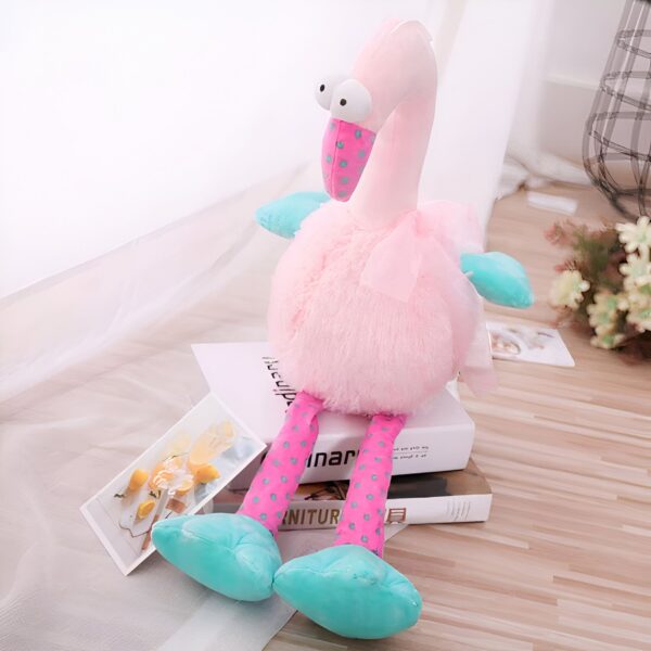 peluche-flamant-rose-rigolote-1a-2 Une peluche de flamant rose avec de grands yeux, un corps rose duveteux, des pieds bleus et des points bleus sur ses jambes.