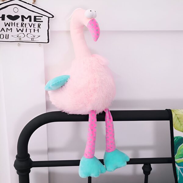 peluche-flamant-rose-rigolote-3a Un flamant rose en peluche avec des points roses sur ses pattes, assis sur un cadre de lit noir.