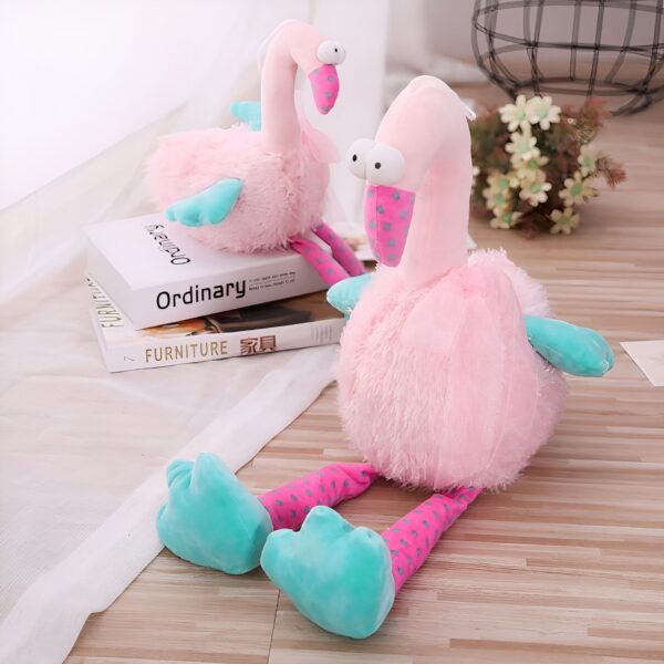 peluche-flamant-rose-rigolote-4a Deux peluches de flamants roses assis sur un sol en bois. Les flamants ont des points roses sur leurs pattes et leurs corps sont en fourrure rose.