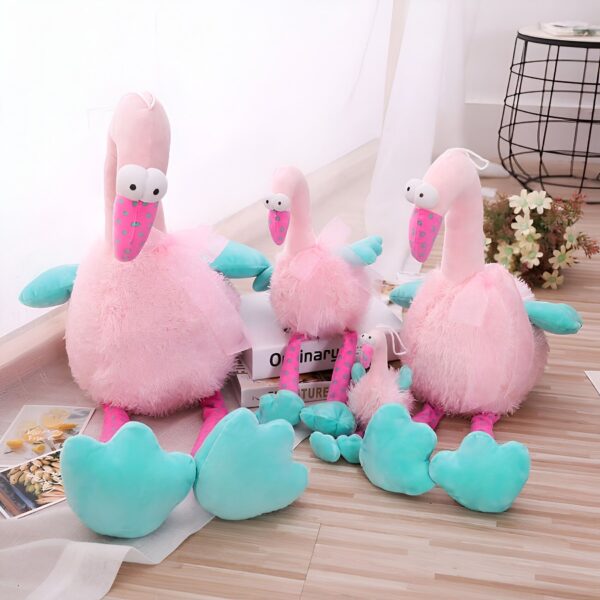 peluche-flamant-rose-rigolote-5a Une famille de trois adorables flamants roses en peluche, assis sur un sol en bois. Le plus grand flamant est assis à gauche, suivi d'un plus petit au centre et d'un tout petit à droite. Ils ont tous des yeux globuleux et des pattes turquoise.