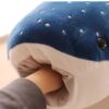 Une peluche en forme de requin-baleine bleu avec des points blancs, une main humaine dans sa bouche.