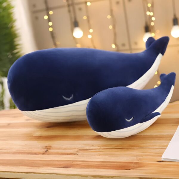 Deux baleines en peluche bleu marine avec des rayures blanches sur un fond en bois.