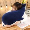 Une jeune femme en lunettes serre dans ses bras une grande peluche baleine bleue.