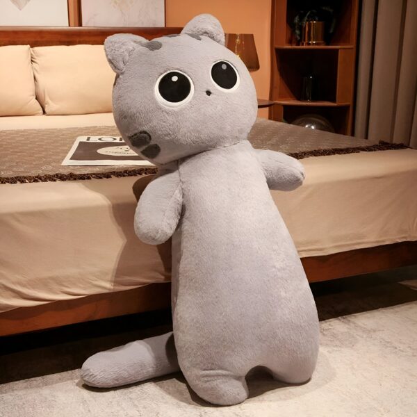 Grande peluche de chat gris posée sur un lit. Le chat a de grands yeux noirs et une expression amusante.