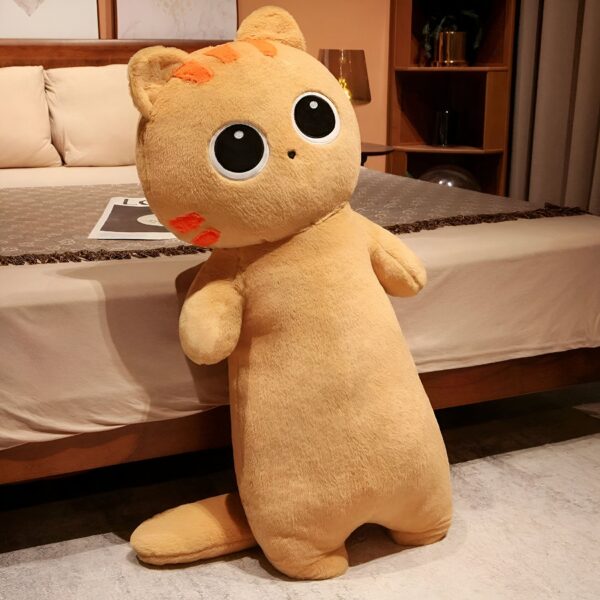 Une peluche de chat beige avec de grands yeux noirs et des moustaches orange debout sur un lit.