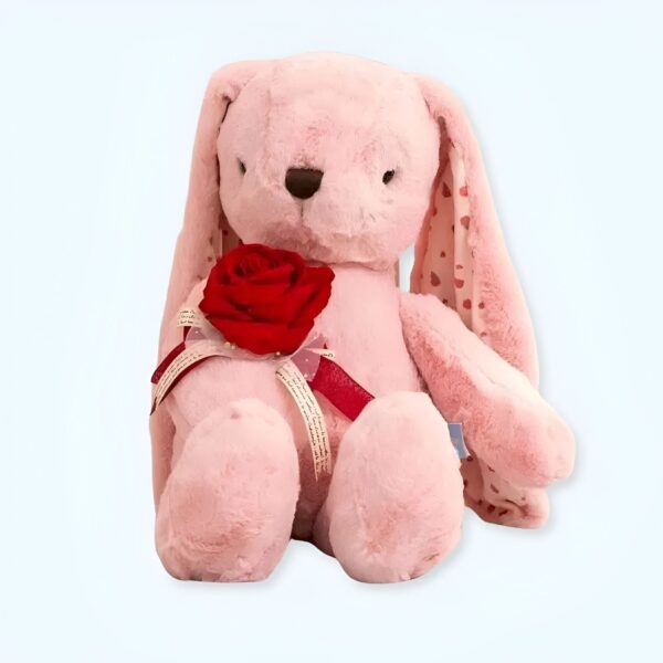 Un lapin rose en peluche assis tenant une rose rouge.