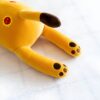 Peluche jaune en forme de chat allongé sur le dos, avec des pattes brunes.
