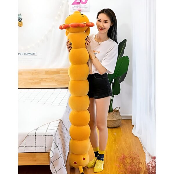 Une jeune femme souriante tenant un long coussin en forme de chenille jaune dans une chambre.
