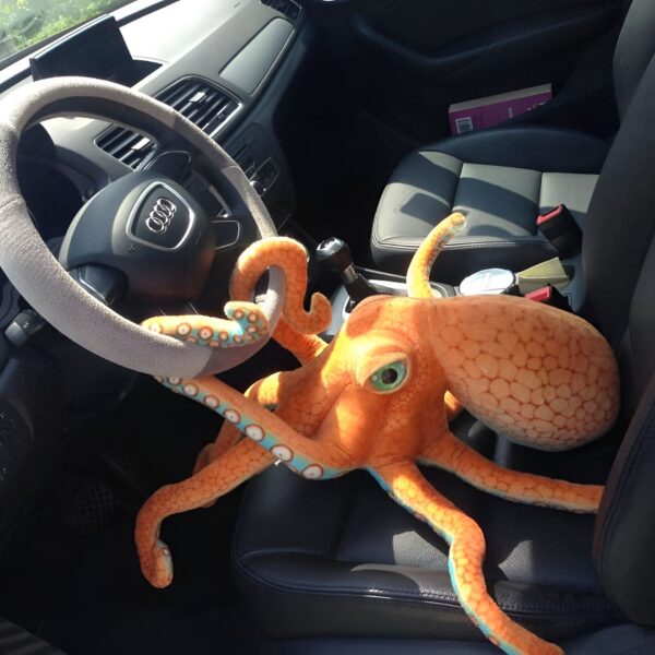 peluche-geante-pieuvre-orange-jouet-doux-enfant-et-adulte-5a-2 Une pieuvre en peluche orange et bleue sur le siège d'une voiture noire.