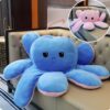 Grande peluche de pieuvre bleue avec un visage triste, assise sur un canapé.