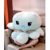 Un gros poulpe en peluche bleu clair avec un visage triste, assis sur un canapé.