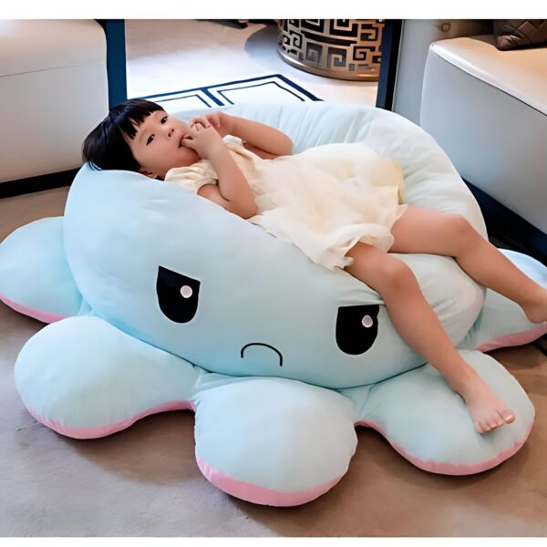 Un enfant assis sur un pouf en forme de pieuvre bleu avec un visage triste.